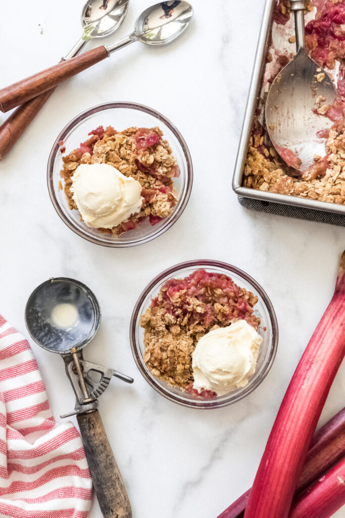 Bowls of rhubarb crisp with ice cream next to an ice cream scoop.