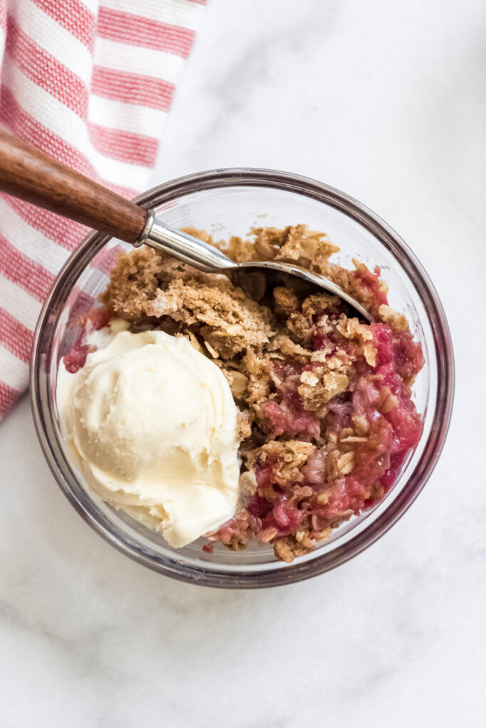 A bowl of rhubarb crisp with a scoop of vanilla ice cream on top.