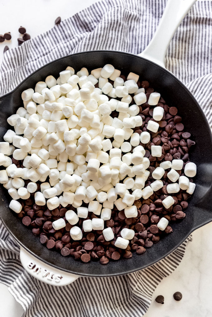 Miniature marshmallows on top of chocolate chips in a cast iron skillet.