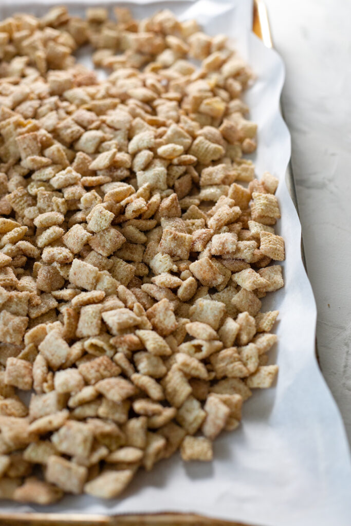 snickerdoodle chex mix on parchment paper lined baking sheet