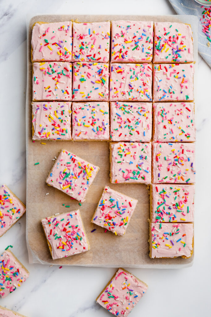 sugar cookie bars with pink frosting and sprinkles cut into bars