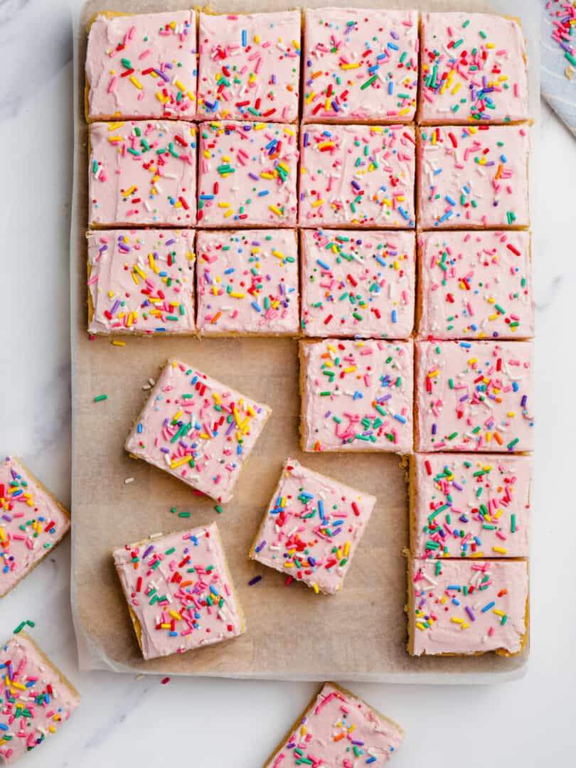 sugar cookie bars with pink frosting and sprinkles cut into bars