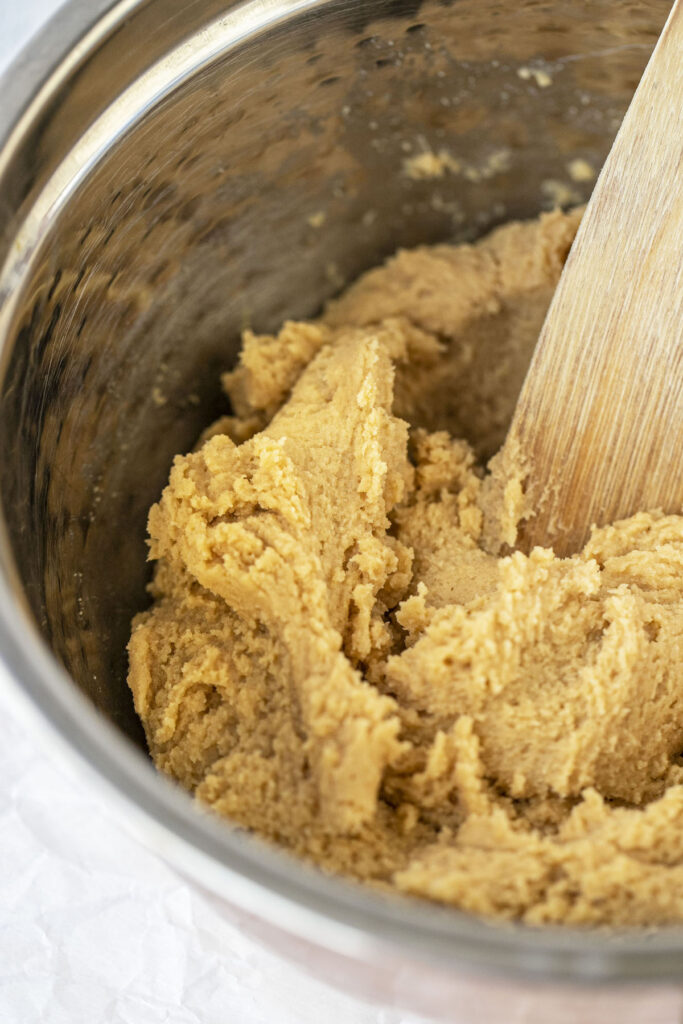 close up of peanut butter cookie dough in a bowl with a wooden spoon