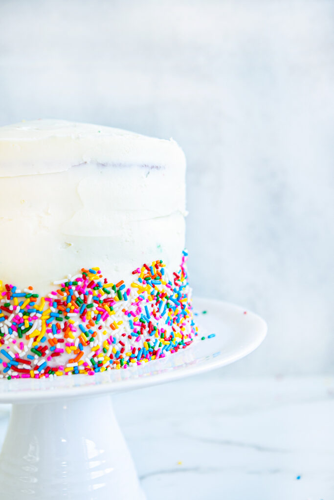 frosted cake with sprinkles on the outside all on a cake stand