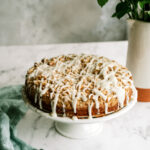 apple crumble cake with icing all on a cake stand