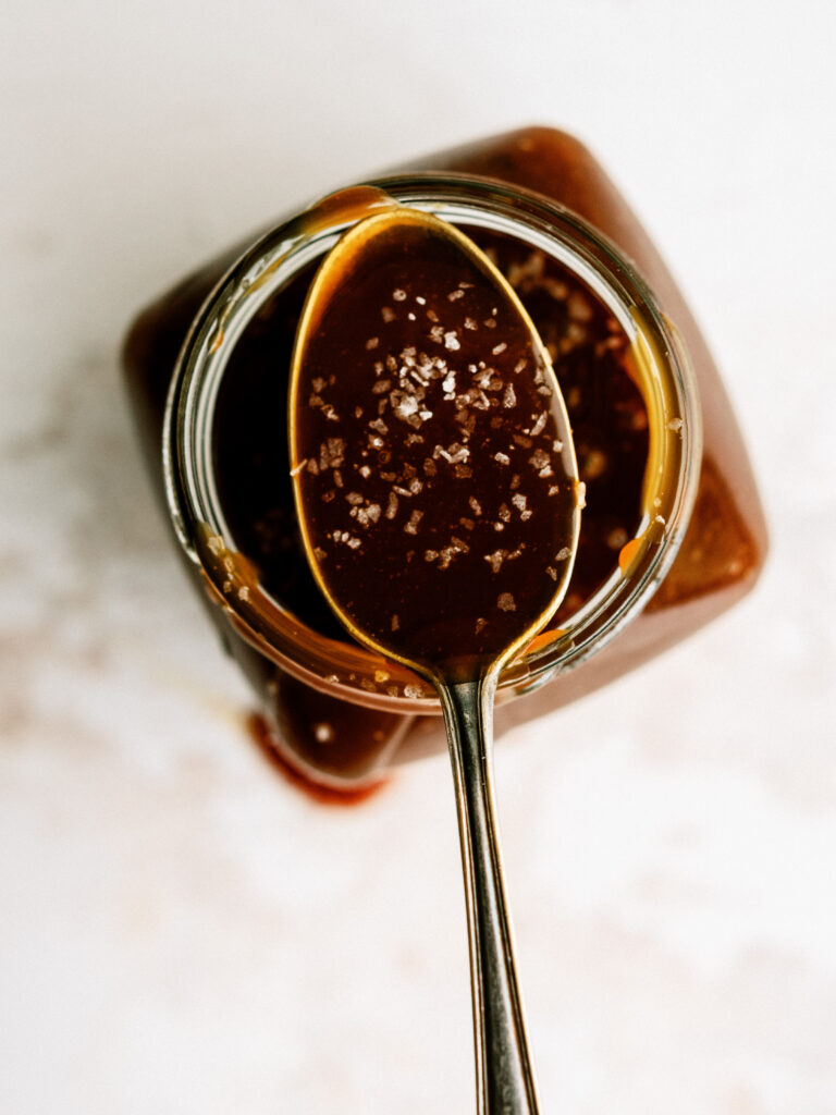 close up of top down view of a spoonful of salted caramel resting on a jar