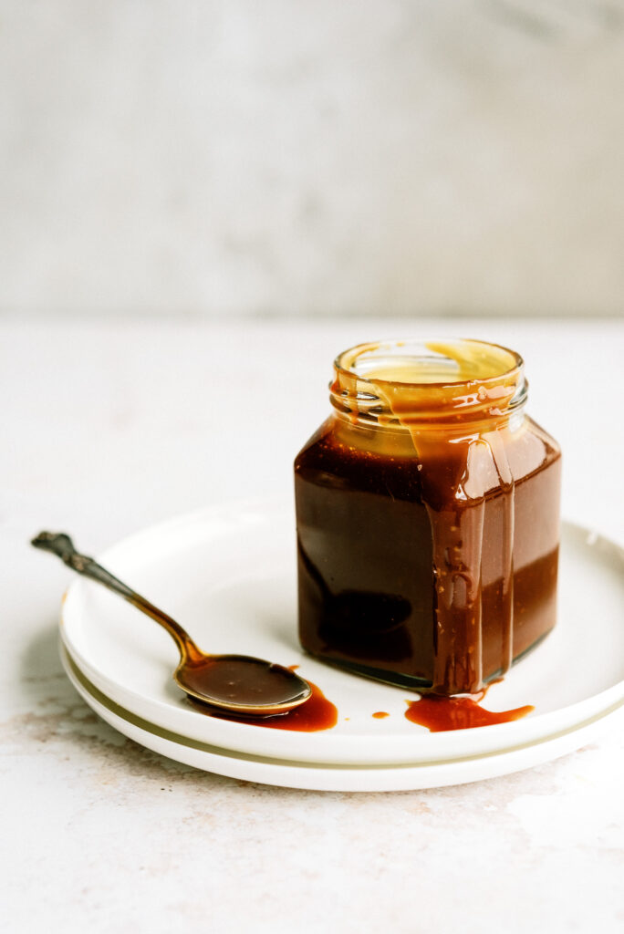 spoon and jar of salted caramel on a stack of white plates