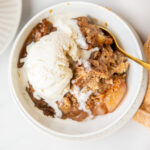 apple dump cake in a white bowl with vanilla ice cream