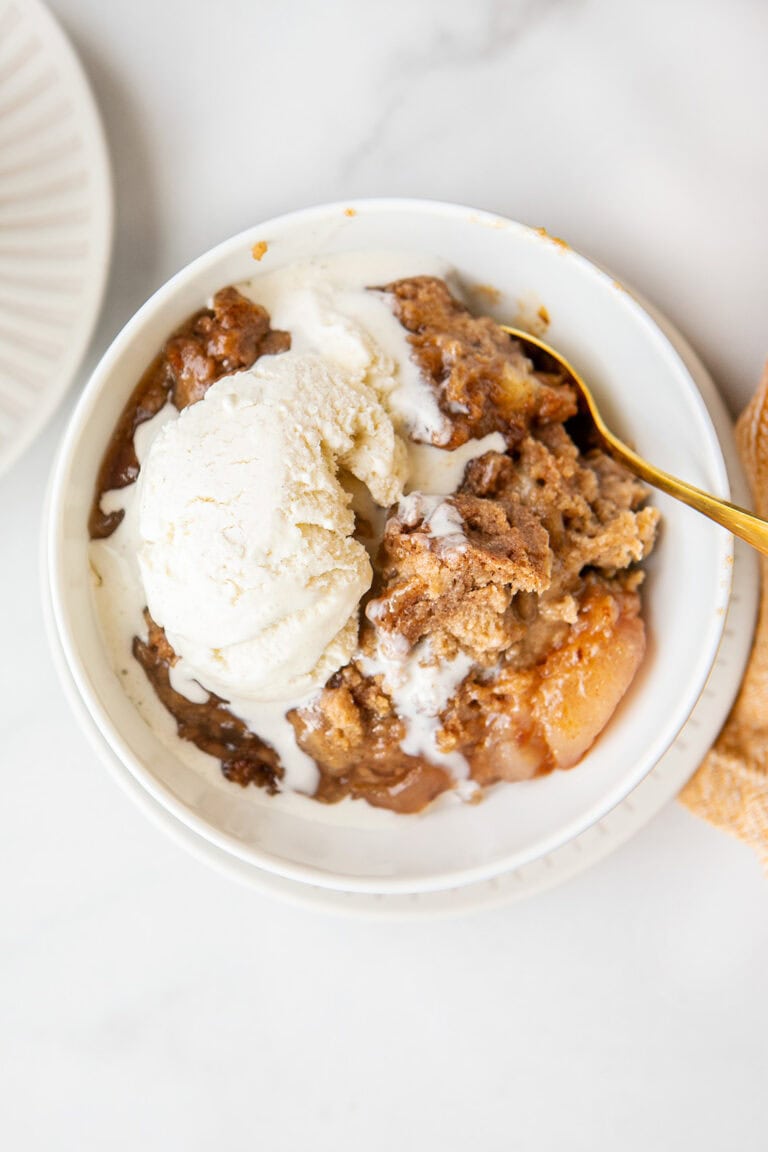 apple dump cake in a white bowl with vanilla ice cream