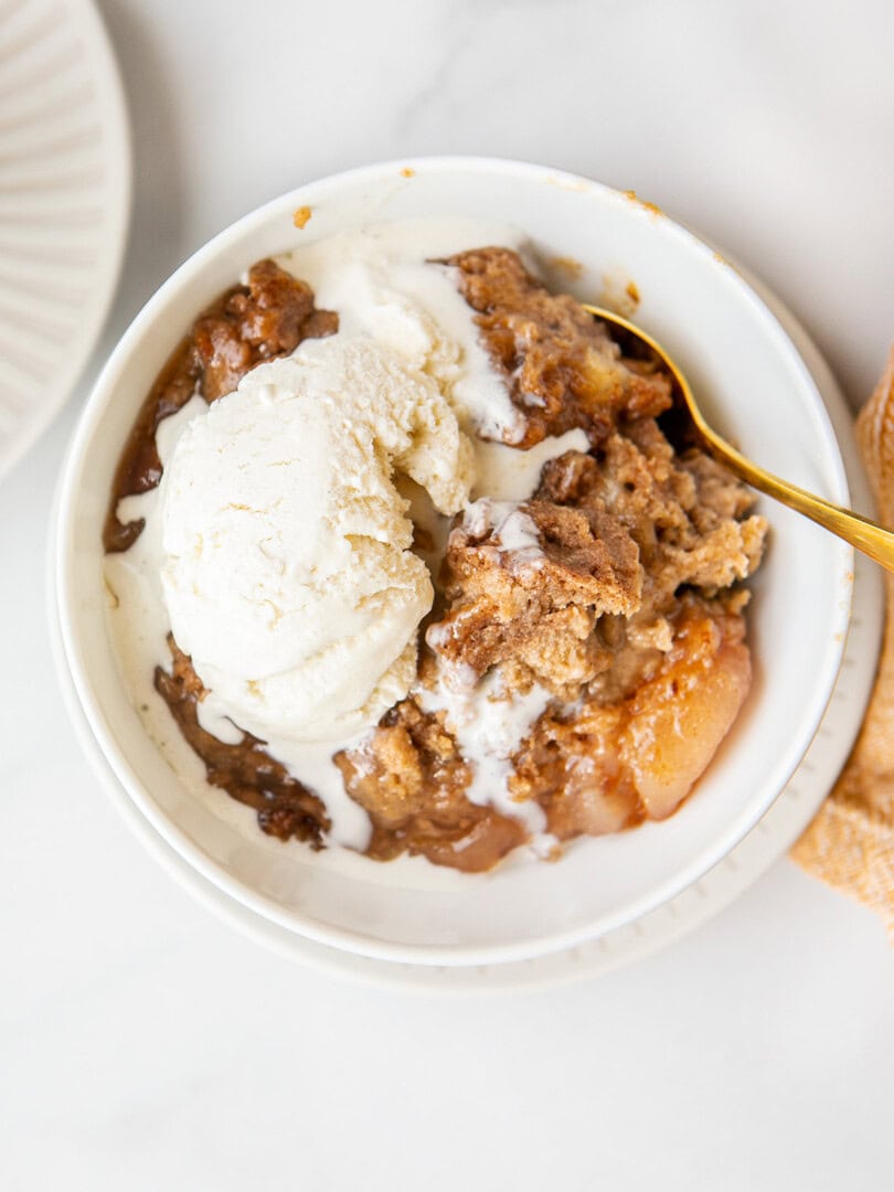 apple dump cake in a white bowl with vanilla ice cream