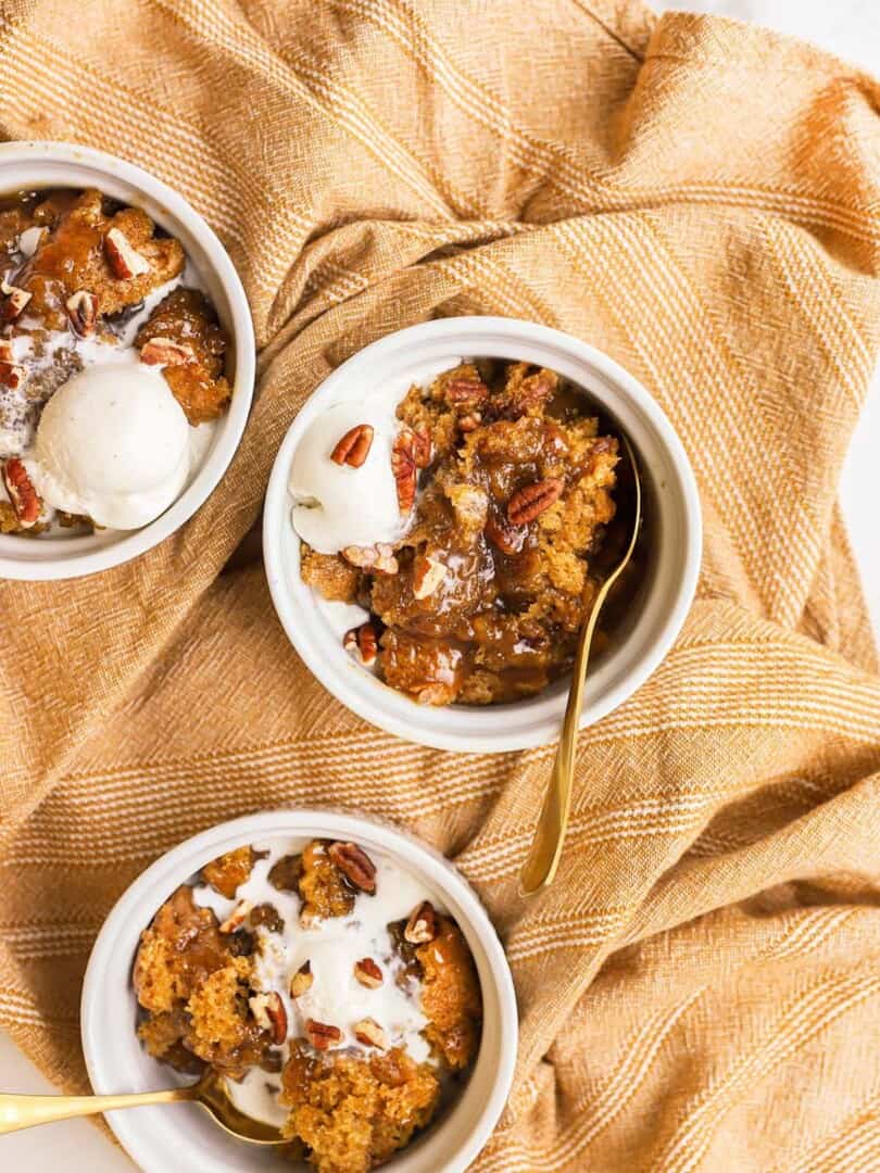 three white bowls with pumpkin cobbler and ice cream in them