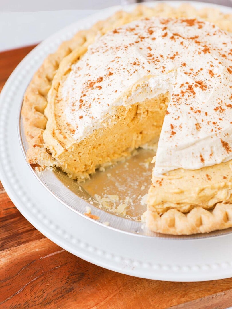 a pie plate full of pumpkin cream pie with a slice taken from it