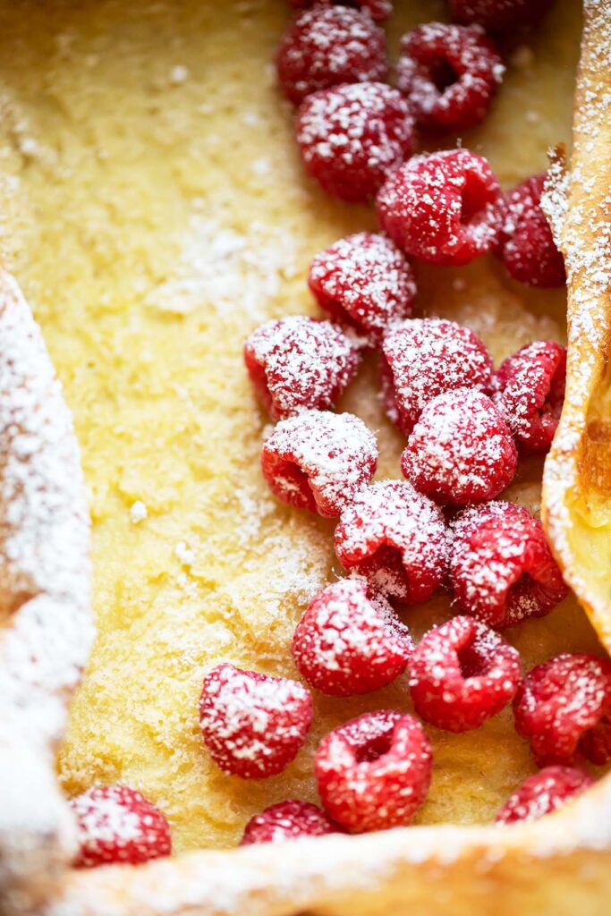 Overhead view of German pancakes in casserole dish topped with fresh raspberries and powdered sugar