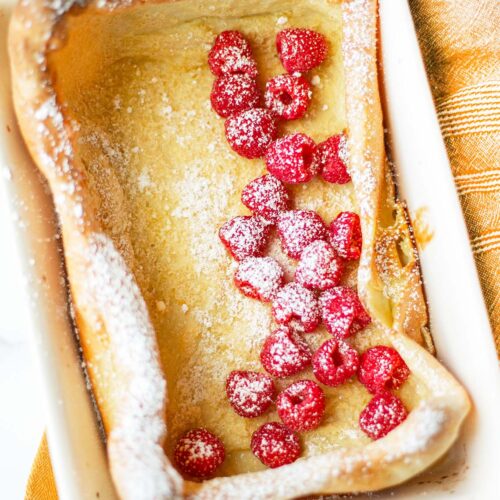 Overhead view of German pancakes in casserole dish topped with fresh raspberries and powdered sugar