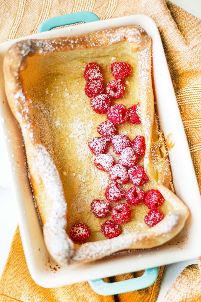 Overhead view of German pancakes in casserole dish topped with fresh raspberries and powdered sugar