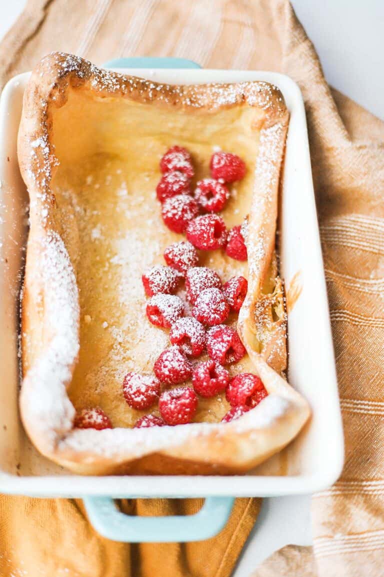 Overhead view of German pancakes in casserole dish topped with fresh raspberries and powdered sugar