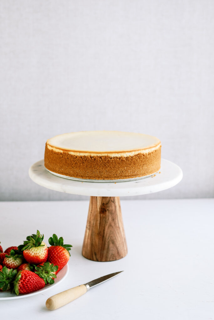 cheesecake on a cake stand with strawberries in a bowl