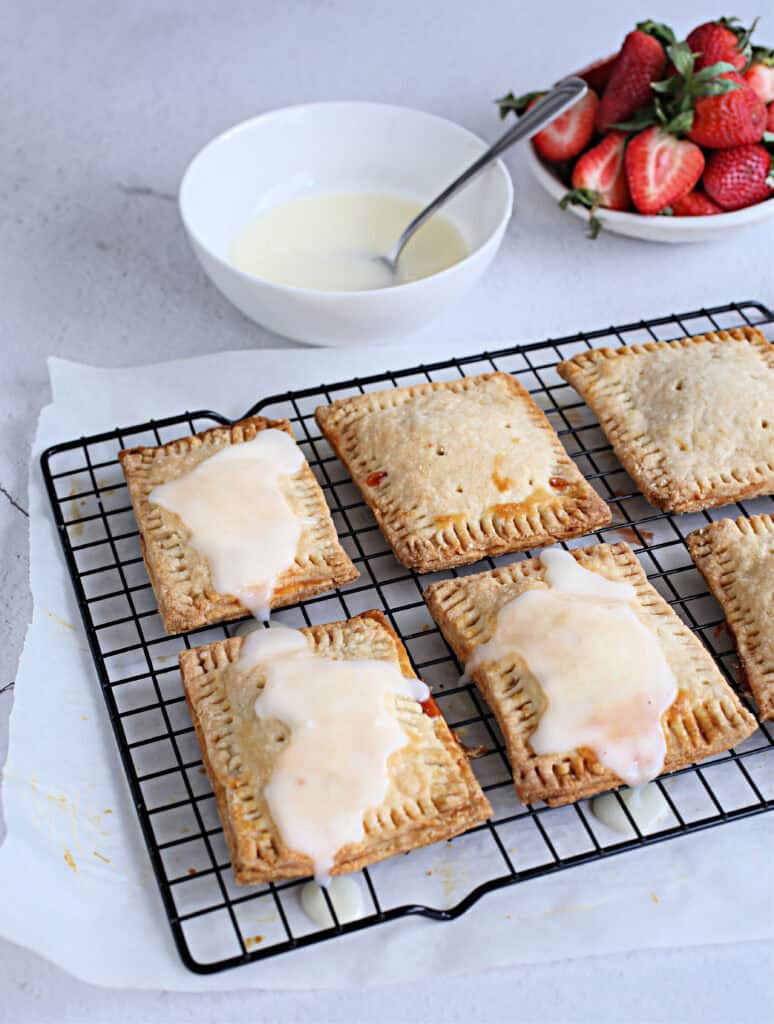 Cooked Pastry squares with strawberry jam filling and glaze on top, on parchment paper.