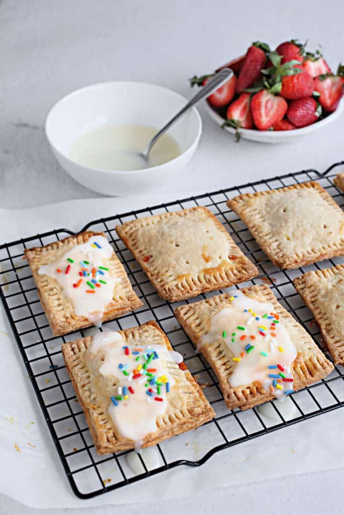 These pastries feature a golden, flaky crust filled with sweet fruit jam, baked to perfection on a parchment-lined tray and topped with glaze and confetti sprinkles.