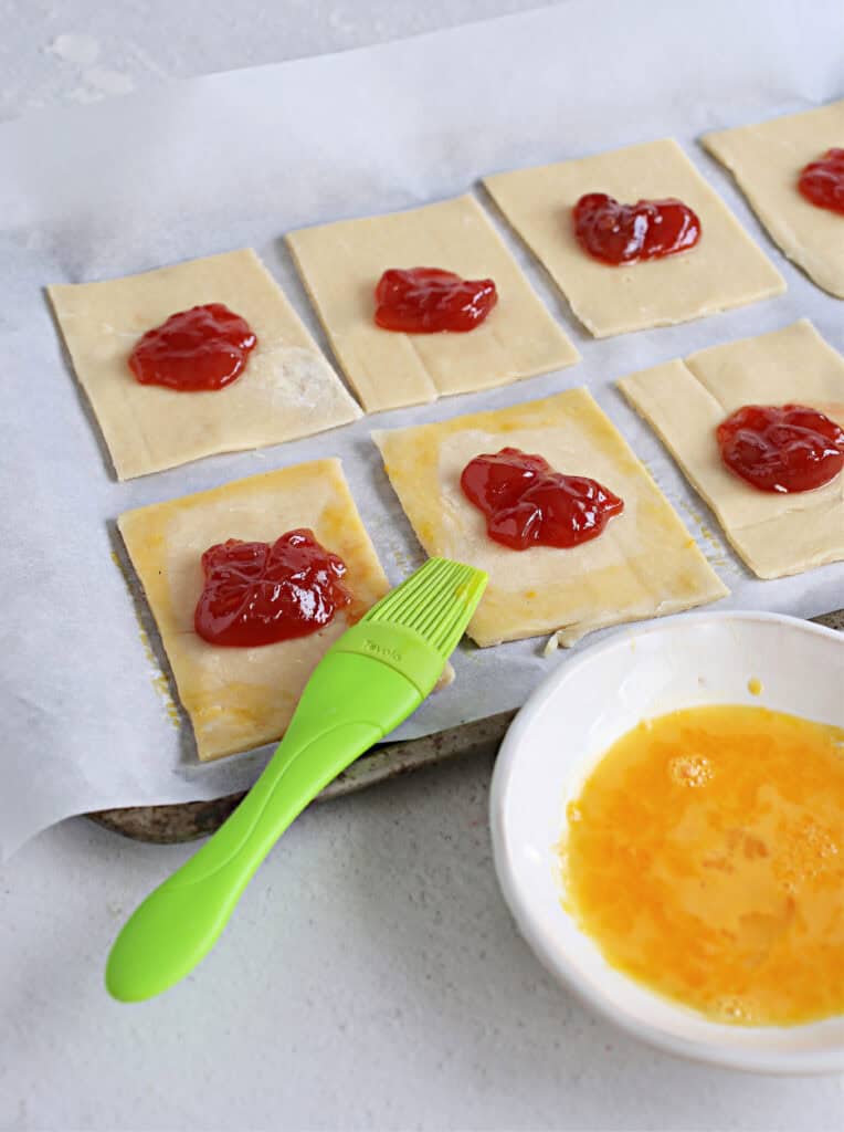 Mini puff pastry squares topped with strawberry jam for a sweet treat.