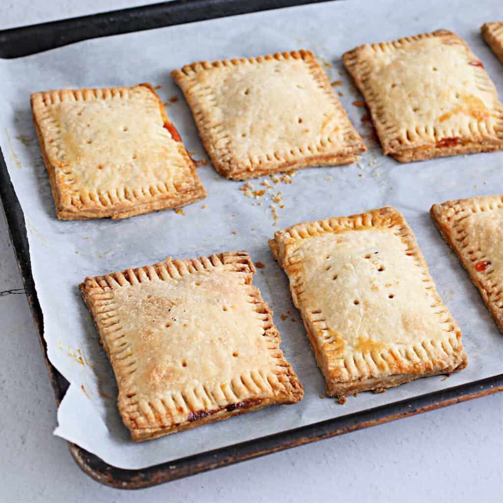 Cooked Pastry squares with strawberry jam filling on parchment paper.